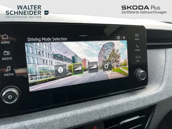 Das Bild zeigt das Innere des Fahrzeugs mit einem Bildschirm, der die Fahrmodusauswahl anzeigt. Die Innenfarbe ist schwarz, und das Händlerlogo ist sichtbar.