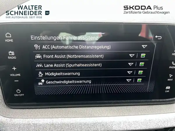 Das Bild zeigt das Innenleben eines ŠKODA Fahrzeugs mit einem Display, das Einstellungen für Fahrassistenzsysteme anzeigt. Das Interieur ist in Schwarz gehalten. Das Händlerlogo ist sichtbar.