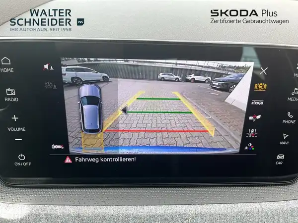 Das Bild zeigt eine Innenaufnahme des Fahrzeugs mit einem Rückfahrkamera-Display. Das Interieur ist schwarz. Es ist ein Händlerlogo sichtbar und es enthält Texteinblendungen.