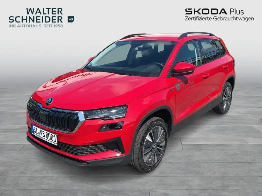 Das Bild zeigt einen roten ŠKODA KAROQ aus der Seitenansicht mit einem Händlerschild im Hintergrund.