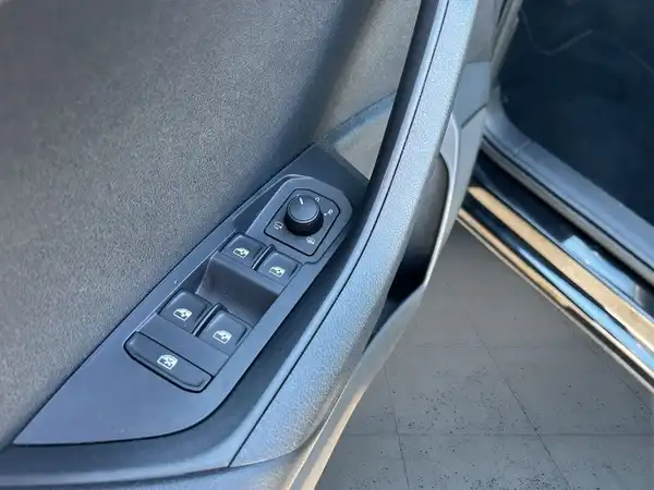Das Bild zeigt die Innenansicht der Türverkleidung eines ŠKODA KAROQ mit Bedienelementen für Fensterheber und Spiegel. Die Farbe des Innenraums ist schwarz.