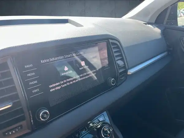 Das Bild zeigt den Innenraum eines ŠKODA KAROQ, insbesondere das Armaturenbrett mit einem eingebauten Display in Schwarz.