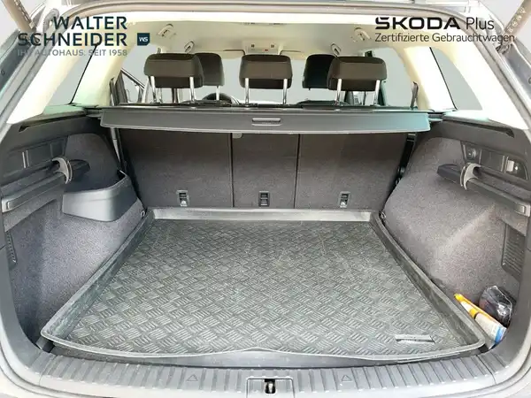 Das Bild zeigt den Innenraum des Kofferraums eines ŠKODA KODIAQ. Es ist eine Innenaufnahme in schwarzer Farbe, auf dem Foto sind das Händlerinformationen und ein Logo sichtbar.