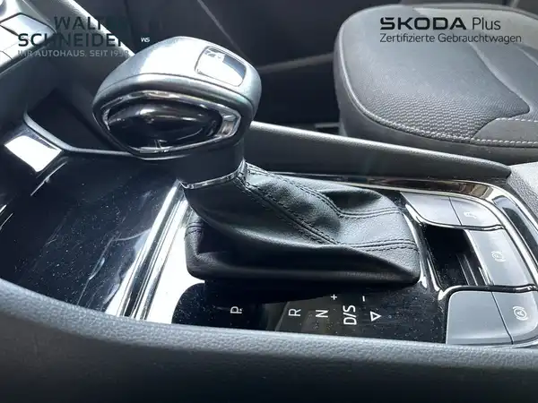 Das Bild zeigt eine Innenaufnahme des Fahrzeugs, speziell den Schalthebel und die Mittelkonsole. Das Interieur ist schwarz. Das Händlerlogo ist ebenfalls sichtbar.