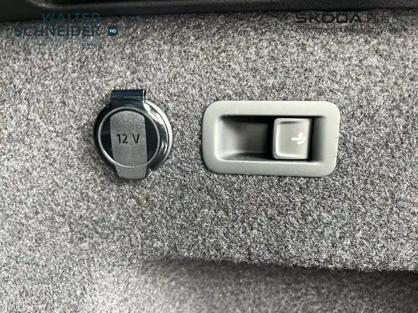Dies ist eine Innenaufnahme des Fahrzeugs, die einen 12-Volt-Anschluss und einen Hebel zeigt. Der Innenraum ist grau und das Händlerlogo ist sichtbar.