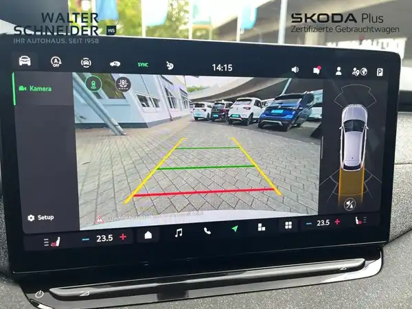 Innenaufnahme des Fahrzeugs mit schwarzem Interieur. Die Anzeige zeigt eine Rückfahrkamera mit Markierungen und Fahrzeugansicht. Händlerinformationen sind eingeblendet.