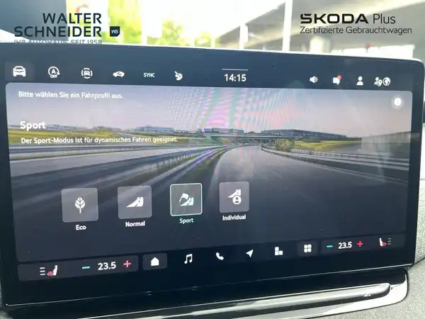Innenaufnahme des Fahrzeugs, zeigt einen Bildschirm mit verschiedenen Fahrmodi und Einstellungen. Das Fahrzeug hat ein schwarzes Interieur. Auf dem Bildschirm sind markante Textinformationen und das Händlerlogo sichtbar.