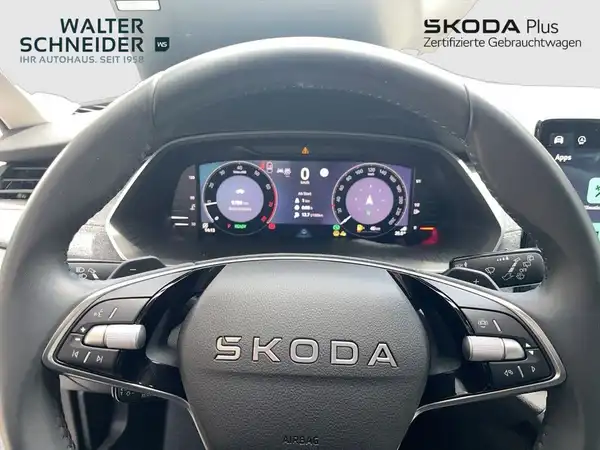 Das Bild zeigt das Innere eines ŠKODA OCTAVIA mit einem Blick auf das Lenkrad und das digitale Cockpit. Der Innenraum ist schwarz. Auf dem Bild sind Händlerlogos und markante Texteinblendungen zu sehen.