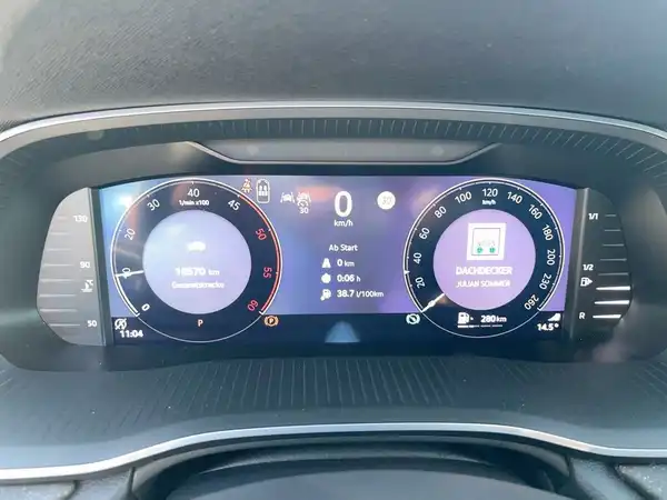 Das Bild zeigt das Innenleben eines Fahrzeugs, eine Aufnahme des Armaturenbretts mit einem digitalen Display. Das Interieur ist schwarz und es sind markante Texteinblendungen im Display zu sehen.