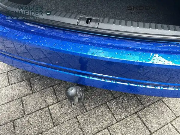 Das Bild zeigt den Kofferraum eines blauen ŠKODA OCTAVIA aus der Rückansicht. Es sind Wassertropfen auf der Oberfläche sichtbar. Das Händlerinformationslogo ist eingeblendet.