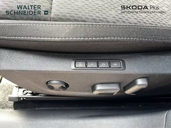 Das Bild zeigt eine Innenaufnahme des ŠKODA OCTAVIA, speziell den Bereich zur Einstellung des Fahrersitzes. Die Farbe des Interieurs ist schwarz. Oben links ist das Händlermarke abgebildet.