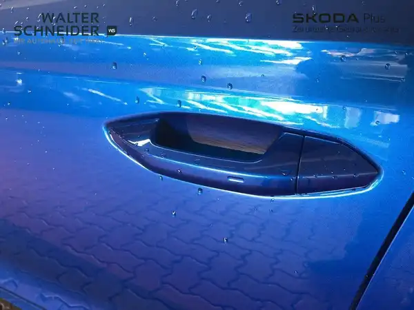 Das Bild zeigt die Tür eines blauen ŠKODA OCTAVIA aus der Seitenansicht mit sichtbarem Händlertlogo und einigen Wassertropfen auf der Oberfläche.