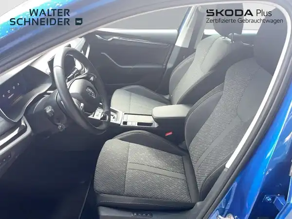 Es handelt sich um eine Innenaufnahme des Fahrzeuges, das blau ist. Die Sitze und das Interieur sind schwarz. Das Händlerlogo ist sichtbar und das Bild enthält markante Texteinblendungen.
