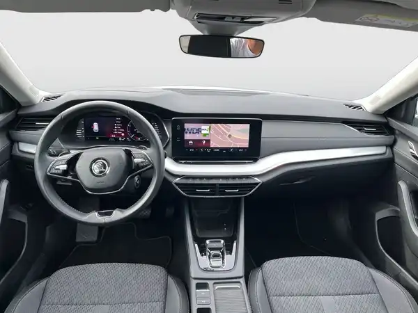 Das Bild zeigt das Innere eines ŠKODA OCTAVIA mit einem schwarzen Armaturenbrett und grauen Stoffpolstern. Zu sehen ist das Lenkrad und ein Infotainment-Bildschirm.