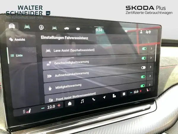 Das Bild zeigt das Innere eines ŠKODA OCTAVIA RS mit einem Screenshot des Displays, das die Einstellungen für die Fahrassistenz anzeigt. Der Innenraum ist in Schwarz gehalten und das Händlerlogo ist eingeblendet.
