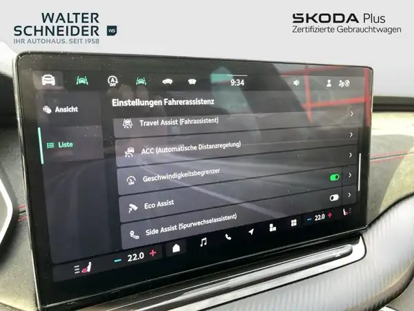 Das Bild zeigt den Innenraum eines ŠKODA-Fahrzeugs, speziell den Bildschirm mit Einstellungen für die Fahrerassistenz. Der Innenraum ist schwarz, und es sind Händlerlogos sowie markante Texteinblendungen sichtbar.