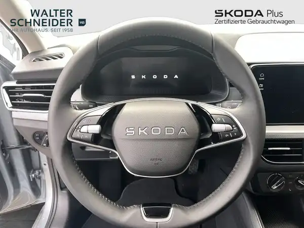 Das Bild zeigt das Innere eines ŠKODA Fahrzeugs mit einem schwarzen Lenkrad und Armaturenbrett. Es sind die Logos des Händlers Walter Schneider sowie SKODA Plus sichtbar.
