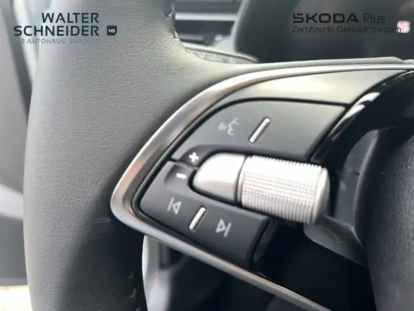 Nahaufnahme des Innenraums eines ŠKODA Fahrzeugs, insbesondere des Lenkrads und der Bedienelemente. Das Bild enthält das Händlerlogo und markante Texteinblendungen.