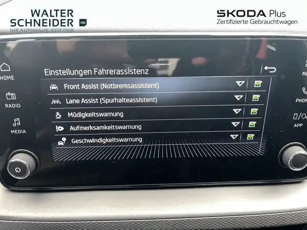 Das Bild zeigt das Innere eines ŠKODA Fahrzeugs, fokussiert auf die Einstellungen des Fahrerassistenzsystems. Das Händlersymbol von Walter Schneider ist sichtbar und es sind markante Texteinblendungen zu den Funktionen vorhanden.
