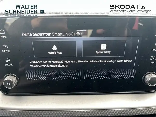 Innenaufnahme des Fahrzeugs, die das Infotainment-System zeigt. Es sind händlerlogos sowie markante Texteinblendungen sichtbar.