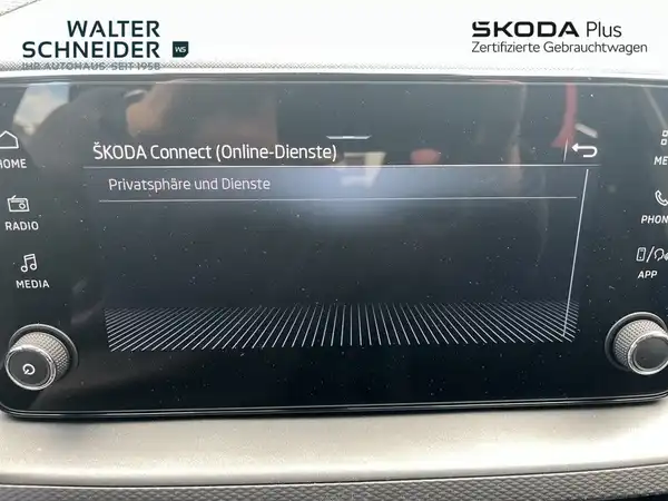 Das Bild zeigt das Innere eines ŠKODA Fahrzeugs, insbesondere den Bildschirm mit SKODA Connect (Online-Dienste). Es ist eine Innenaufnahme, die in einem modernen schwarzen Interieur gehalten ist.