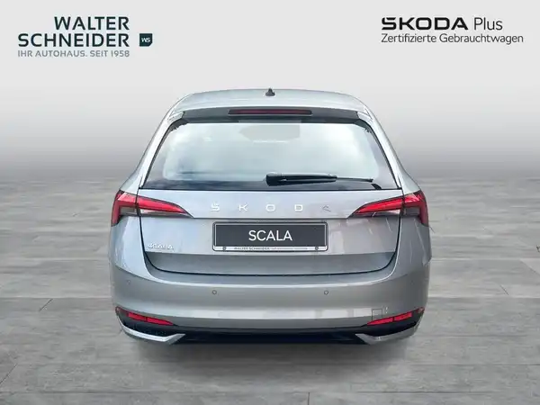 Das Bild zeigt einen silbernen ŠKODA SCALA aus Rückansicht, aufgenommen vor einem einfarbigen Hintergrund. Auf dem Bild sind die Logos des Händlers und der Marke zu sehen.