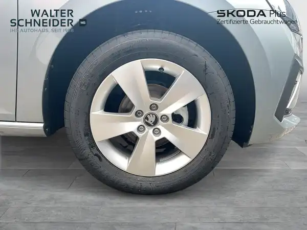 Das Bild zeigt die Seite eines silbernen ŠKODA Fahrzeugs, speziell das Rad und die Felge, mit sichtbarem Händlerlogo und zusätzlichem Text.