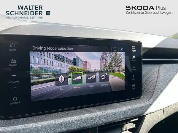 Das Bild zeigt den Innenraum eines ŠKODA-Fahrzeugs mit einem Display zur Auswahl des Fahrmodus. Der Innenraum ist in Grau gehalten und das Händlerinlogo ist sichtbar.