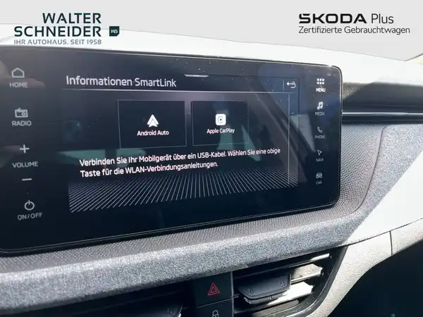Innenaufnahme des Fahrzeugs, zeigt das Infotainment-System mit Android Auto und Apple CarPlay Optionen. Die Interieurfarbe ist grau. Händlerlogo ist sichtbar und das Bild enthält markante Texteinblendungen.