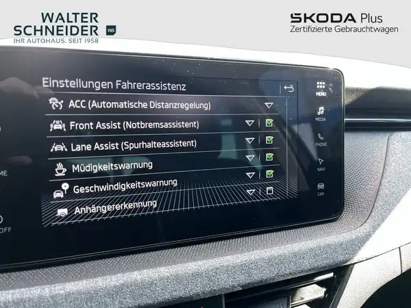 Innenaufnahme des Fahrzeugs mit einem Display, das Einstellungen für Fahrassistenz zeigt. Das Interieur ist schwarz, das Händlerlogo ist sichtbar.
