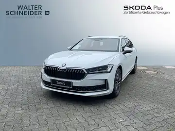 Das Bild zeigt einen weißen ŠKODA SUPERB aus der Frontansicht. Im Hintergrund sind Händlerlogos sichtbar.