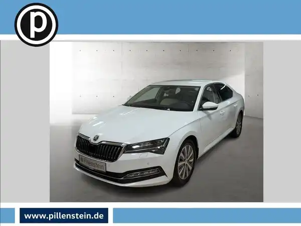 Das Bild zeigt einen weißen ŠKODA SUPERB aus der Frontansicht. Das Händlersymbol ist vorhanden und es gibt markante Texteinblendungen.