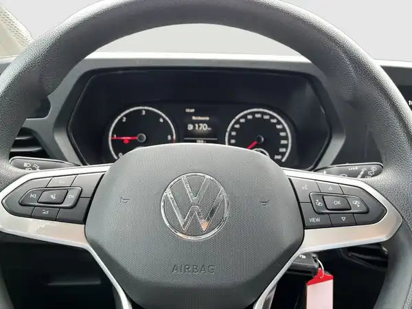 Das Bild zeigt das Innere eines VW CADDY, insbesondere das Lenkrad und das Armaturenbrett. Es ist eine Innenaufnahme in schwarzer Farbe.