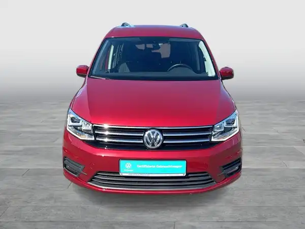 Das Bild zeigt einen roten Volkswagen Caddy, aufgenommen von vorne. Es enthält markante Texteinblendungen.