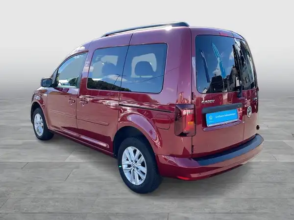 Das Bild zeigt einen roten VW Caddy von der Seite, aufgenommen aus einem schrägen Winkel. Auf dem Fahrzeug ist ein markanter Text sichtbar.