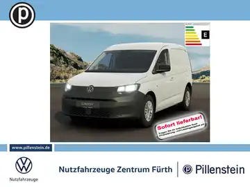 Ein Bild eines weißen VW Caddy, aufgenommen von vorne. Im Hintergrund sind Berge und eine klare Himmel zu sehen. Es enthält das Händlerlogo und einen auffälligen Text mit der Aufschrift 'Sofort lieferbar'.