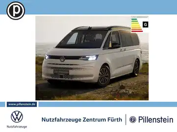 Das Bild zeigt einen weißen VW California Beach, aufgenommen von vorne. Es enthält ein Händlerlogo und markante Texteinblendungen.