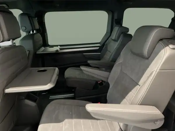Das Bild zeigt den Innenraum eines VW Multivan mit grauen Sitzen und einem Tisch zwischen den Sitzen.