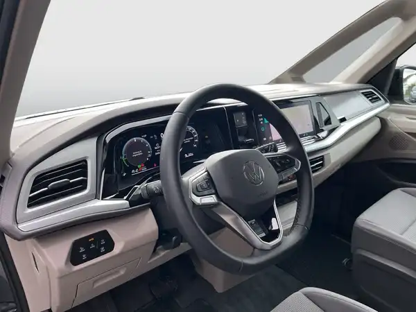 Das Bild zeigt das Innere eines VW Multivan, aus der Perspektive des Fahrers. Die Interieurfarbe ist hellgrau und das gesamte Armaturenbrett sowie das Lenkrad sind sichtbar.