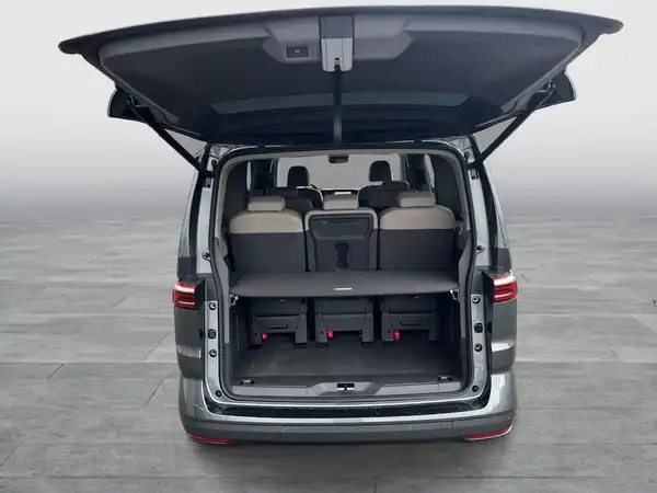 Dies ist ein Bild des VW Multivan von hinten mit geöffnetem Kofferraum, der einen Blick auf die beige Innenausstattung bietet.