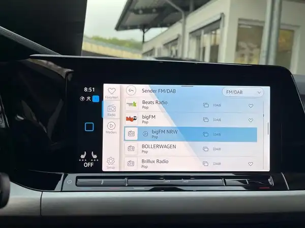 Das Bild zeigt den Innenraum eines VW Golf, insbesondere das Display des Infotainmentsystems. Das Interieur ist schwarz und es sind verschiedene Radiostationen auf dem Bildschirm angezeigt.