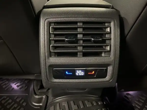 Das Bild zeigt eine Innenaufnahme des Fahrzeugs, speziell die Lüftungsregelung auf dem Rücksitz. Der Innenraum ist schwarz und es sind markante Texteinblendungen zur Temperaturregelung sichtbar.