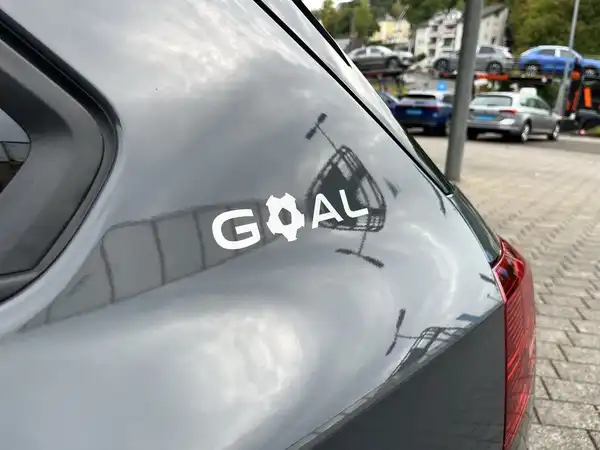 Das Bild zeigt die Rückansicht eines grauen VW Golf Variant mit einem Aufkleber mit der Aufschrift 'GOAL'.
