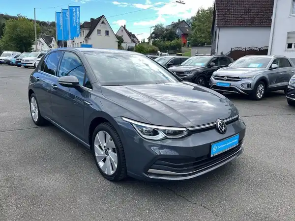Das Bild zeigt einen grauen VW Golf von der Seite, aufgenommen auf einem Parkplatz mit anderen Fahrzeugen im Hintergrund.