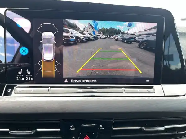 Das Bild zeigt den Innenraum eines Fahrzeugs mit einem Navigationsdisplay, das eine Rückfahrkameraansicht anzeigt.