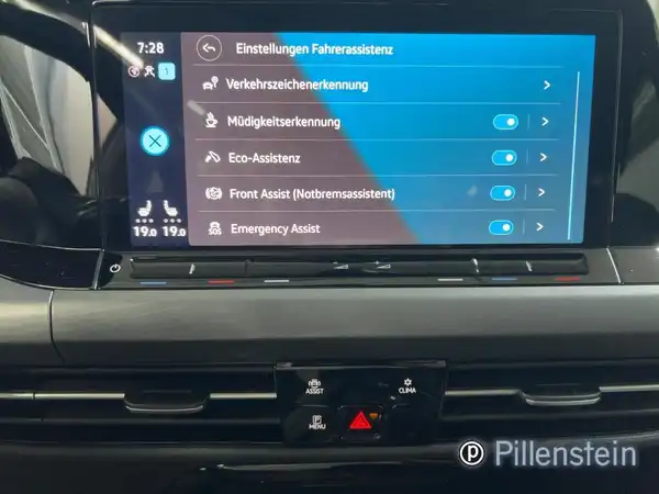 Das Bild zeigt das Innenleben eines VW Golf mit einem Display, das Einstellungen für Fahrassistenzsysteme anzeigt. Die Interieurfarbe ist schwarz und es gibt einen Händlerlogo auf dem Bild.
