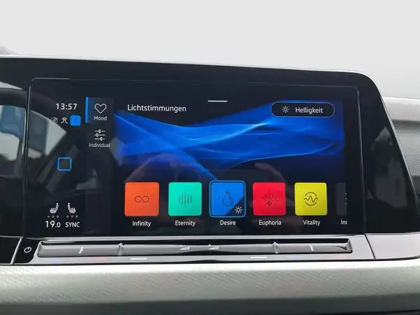 Das Bild zeigt das Innenleben eines Fahrzeugs mit einem Display, das Lichtstimmungen anzeigt. Das Interieur ist schwarz, und es sind markante Texteinblendungen auf dem Display zu sehen.