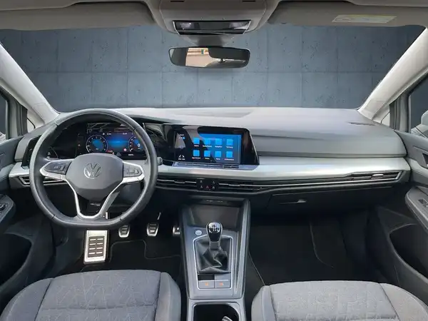 Das Bild zeigt das Innere eines VW Golf, mit einem modernen Armaturenbrett und einem sportlichen Lenkrad. Die Polsterung ist schwarz.