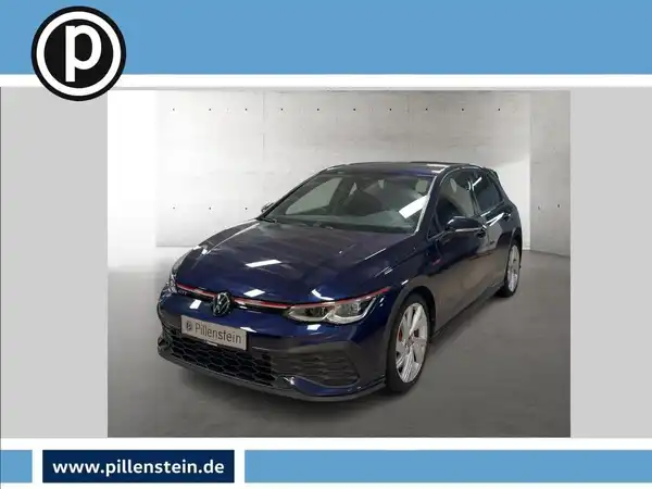 Das Bild zeigt einen blauen VW Golf GTI aus der Frontalansicht. Das Händlersymbol ist in der oberen linken Ecke sichtbar, und es sind markante Texteinblendungen im Bild vorhanden.
