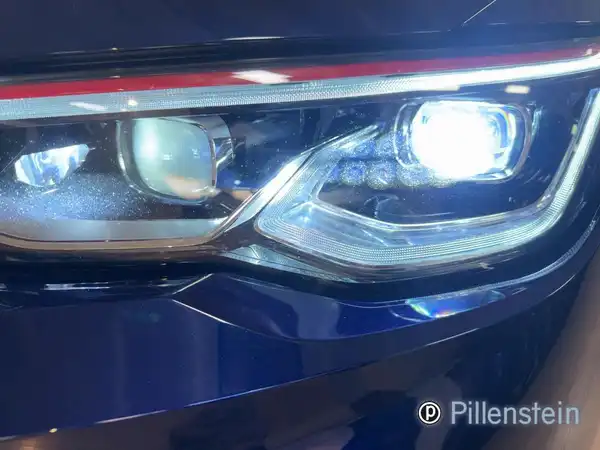 Das Bild zeigt den vorderen Scheinwerfer eines blauen VW Golf GTI, aufgenommen von vorne. Es enthält das Händlerlogo 'Pillenstein'.